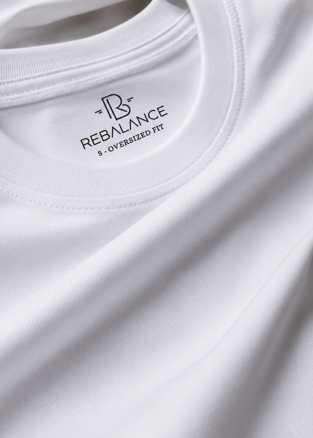 Close-up of a white ribbed knit t-shirt showing the inner neck label with the black REBALANCE logo and 'S - OVERSIZED FIT' text.